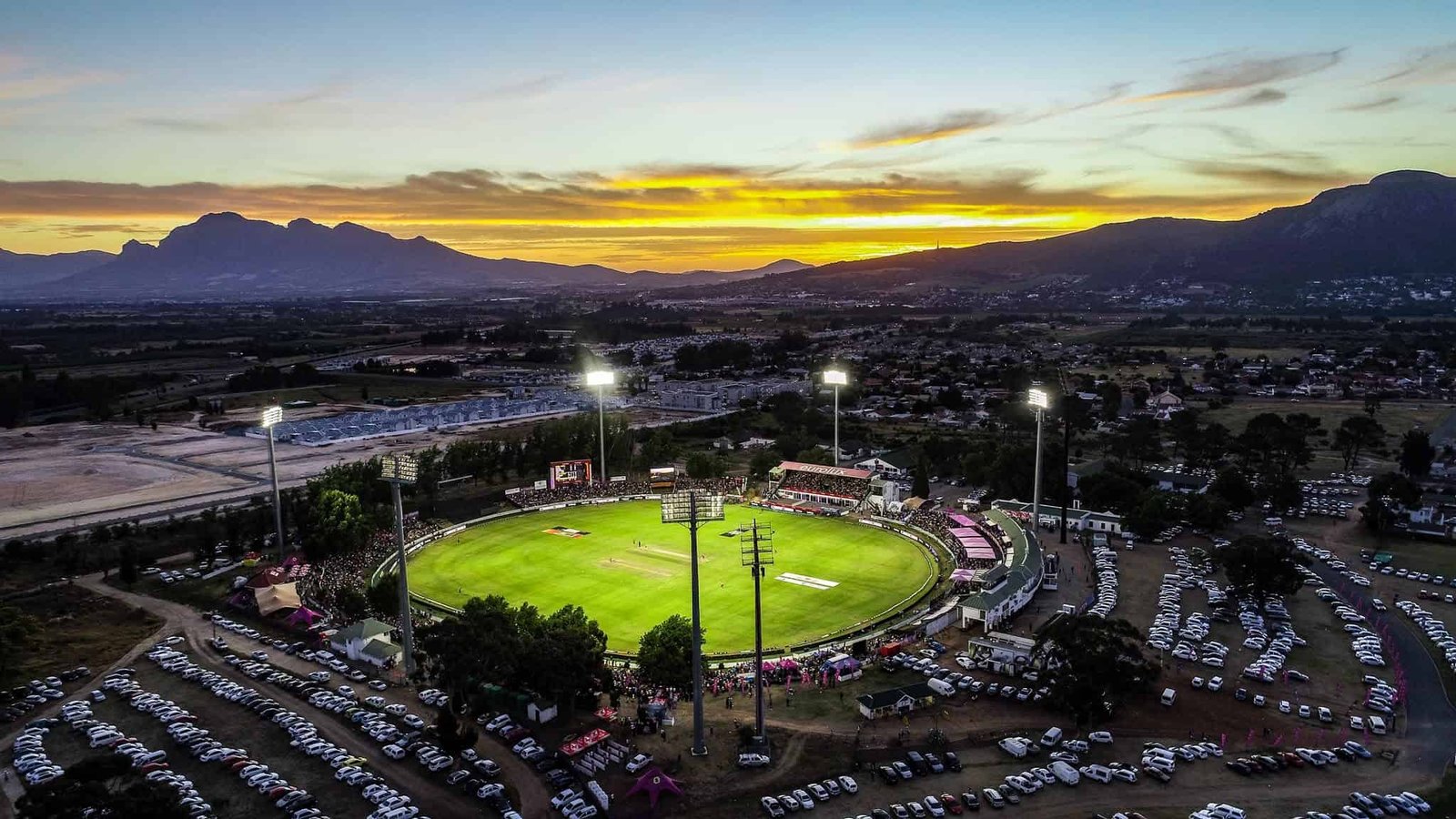 Aerial view of Boland Park in Paarl at sunset, with the illuminated cricket ground and surrounding mountains.