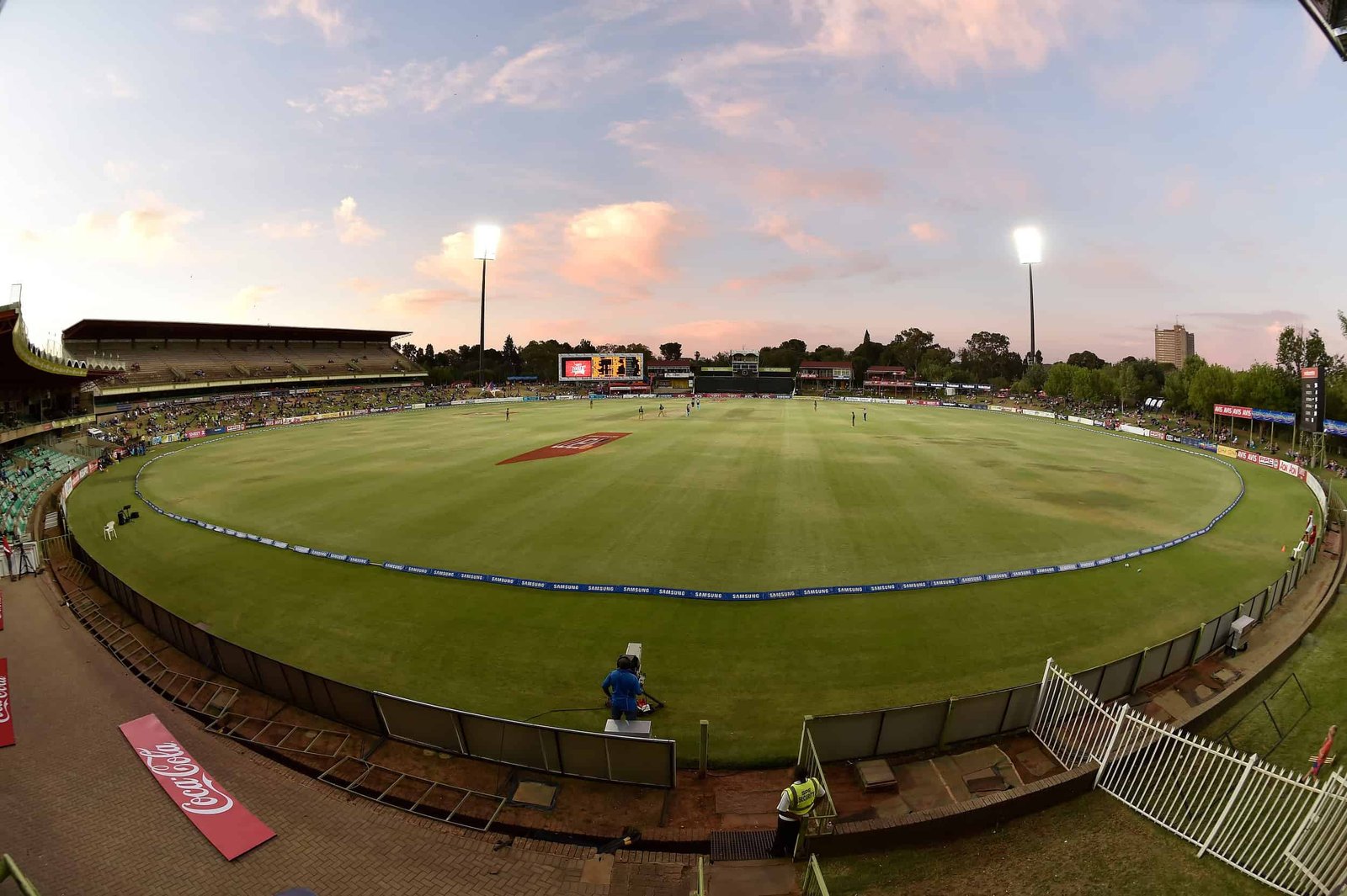 Wide view of Mangaung Oval in Bloemfontein at dusk, with the cricket field, stands and illuminated floodlights.