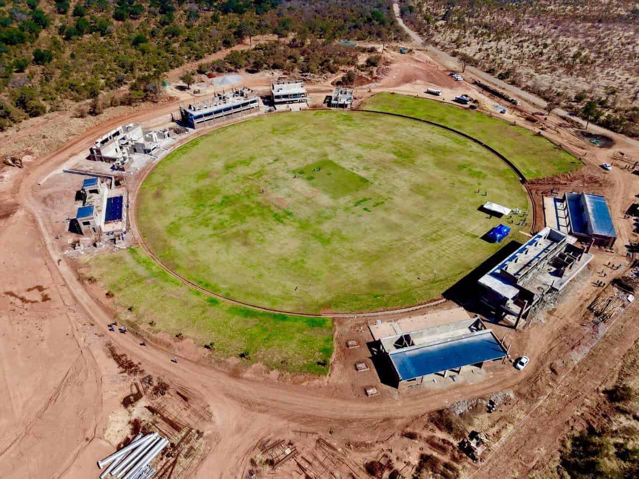 Aerial construction-stage view of Mosi-oa-Tunya International Cricket Stadium in Victoria Falls, showing the grass outfield and unfinished surrounding buildings.