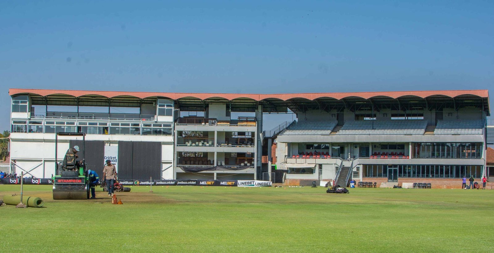 Queens Sports Club in Bulawayo, with ground staff preparing the outfield in front of the pavilion and grandstand.